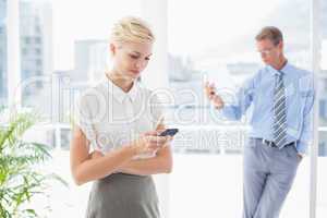 Businesswoman using her smartphone with colleague in background
