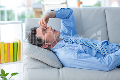 Worried businessman with head in hands lying on couch