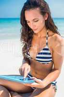 Pretty brunette using tablet pc at the beach