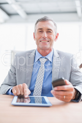 Businessman smiling at camera with his tablet and his phone