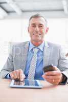 Businessman smiling at camera with his tablet and his phone