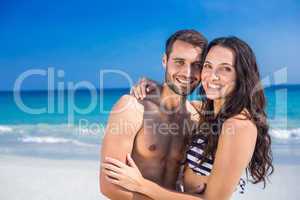 Happy couple embracing at the beach and looking at camera