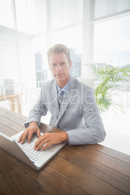 Serious businessman on his laptop looking at camera