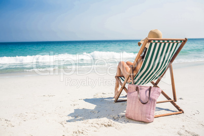 Rear view of pretty brunette relaxing on deck chair at the beach