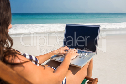 Pretty brunette using laptop on deck chair