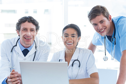 Team of doctors working on laptop and smiling at camera