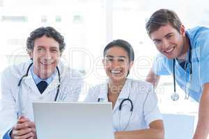 Team of doctors working on laptop and smiling at camera