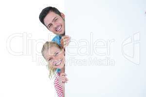 Smiling young couple hiding behind a blank sign