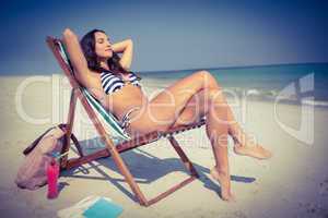 Pretty brunette relaxing on deck chair at the beach