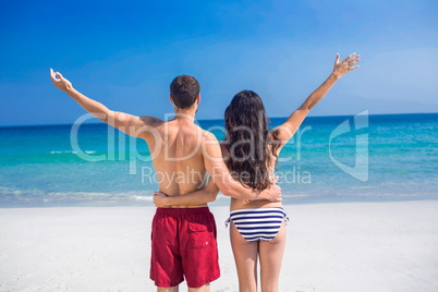 Rear view of happy couple with arms outstretched at the beach