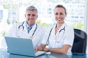 Smiling doctors working together on laptop