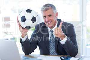 Smiling businessman holding soccer ball with thumbs up
