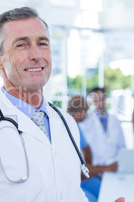 Smiling male doctor looking at camera while his colleagues works