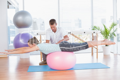 Trainer working with woman on exercise ball