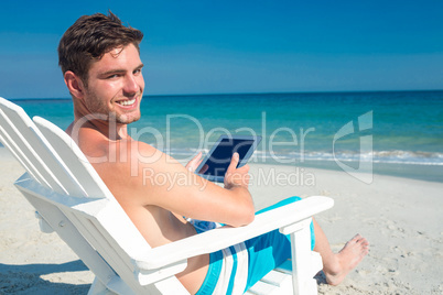 Man using digital tablet on deck chair at the beach