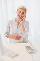 Smiling blonde woman using computer and phoning