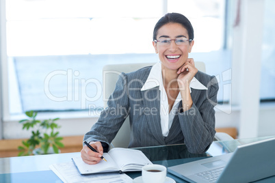 Smiling businesswoman working with her laptop and writing notes