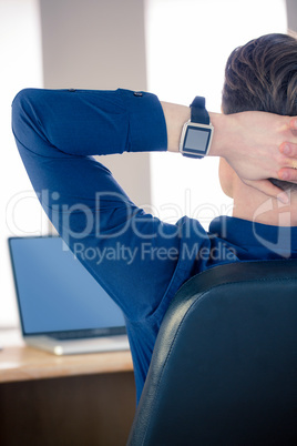 Rear view of businessman relaxing in a swivel chair wearing smar