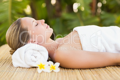 Peaceful blonde lying on bamboo mat with flowers