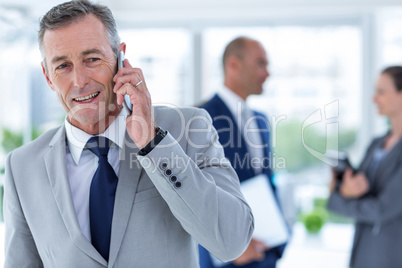 businessman using her phone with two colleague behind him