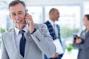 businessman using her phone with two colleague behind him