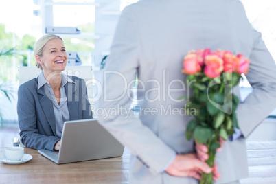 Businessman hiding flowers behind back for colleague