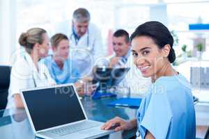 Beautiful smiling doctor typing on keyboard with her team behind