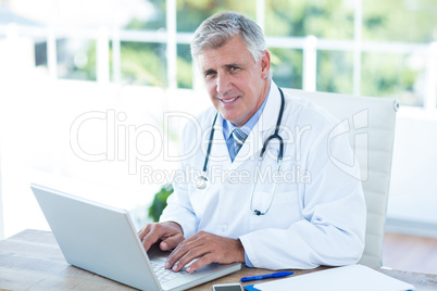 Smiling doctor working on laptop at his desk