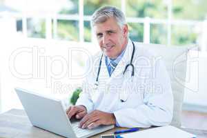 Smiling doctor working on laptop at his desk