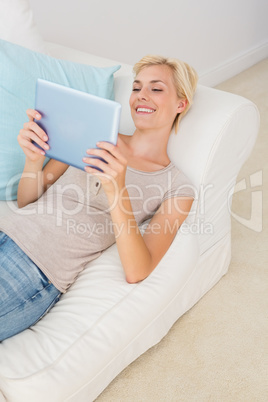 Smiling blonde woman using her digital tablet in the sofa