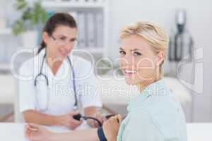 Doctor taking blood pressure of her smiling patient