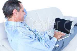 Smiling businessman lying on a sofa holding a laptop
