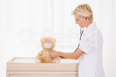 Smiling blonde doctor with stethoscope on the teddy bear
