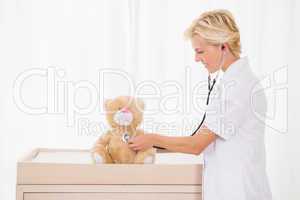 Smiling blonde doctor with stethoscope on the teddy bear
