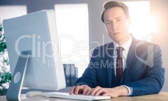 Confident businessman typing on computer and looking at camera