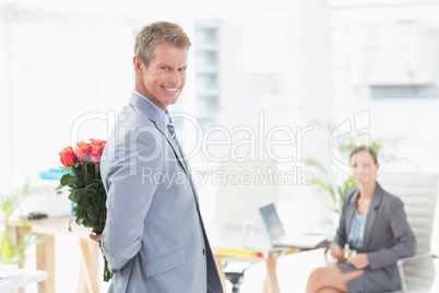 Smiling businessman holding flowers behind his back
