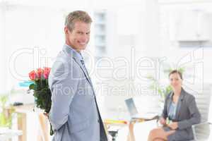 Smiling businessman holding flowers behind his back