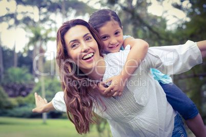 Happy little girl getting a piggy back from mother in the park