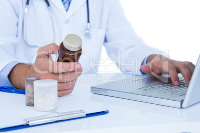 A doctor holding a medecine while typing on a laptop