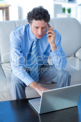 Businessman using laptop and mobile phone on couch