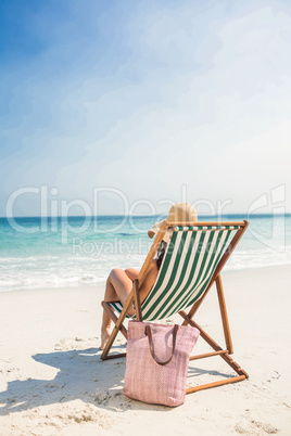 Rear view of pretty brunette relaxing on deck chair at the beach