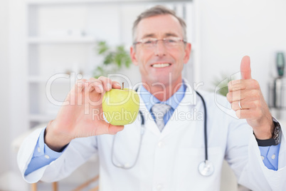 Smiling doctor showing apple with thumbs up