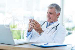 Smiling doctor sitting at his desk and texting