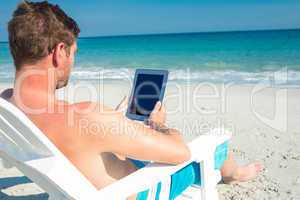 Man using digital tablet on deck chair at the beach