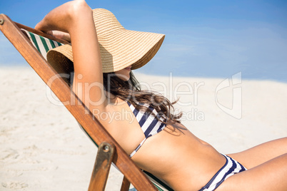 Pretty brunette relaxing on deck chair at the beach