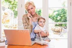 Pretty blonde woman with his son phoning and using laptop