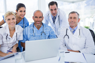 Happy team of doctors looking at camera in behind laptop compute