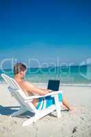 Man using laptop on deck chair at the beach