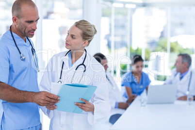 Two doctors looking at clipboard while their colleagues working