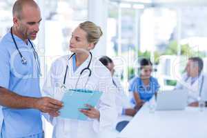 Two doctors looking at clipboard while their colleagues working